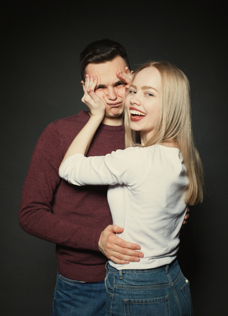 Portrait of a beautiful young couple in love posing at studio over dark background. The girl plays with the face of her boyfriendの写真素材
