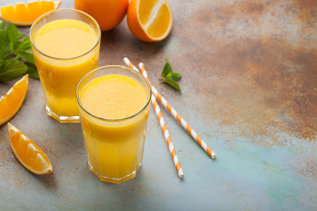 Two glasses with freshly squeezed orange juice and mint on an old rusty blue background. Top view with copy spaceの写真素材