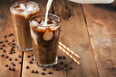 Ice coffee in a tall glass with cream poured over and coffee beans on a old rustic wooden table. Cold summer drink on a dark wooden background with copy space.の写真素材