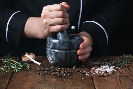 Woman chef pounding spices and herbs in mortar for food cooking on a black background.の写真素材