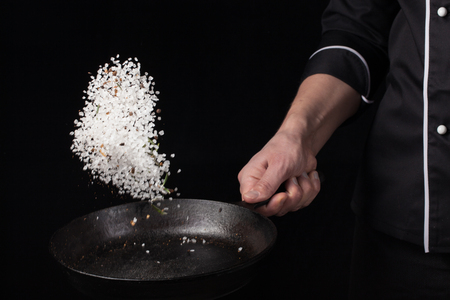 Cooking roasted aromatic salt in a pan by chef hand. Horizontal photo view. Dark black background with copy text area.の写真素材