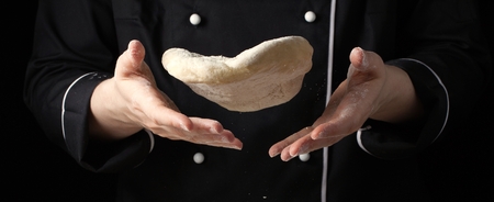 A female cook throws a yeast dough in her hands on a black background.
