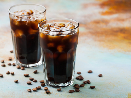 Ice coffee in a tall glass with cream poured over and coffee beans. Cold summer drink on a blue rusty background with copy space.の写真素材