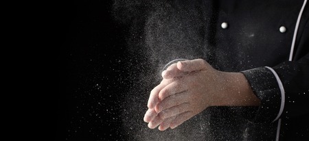 Chef hands in flour on black background banner. Making pizza, pasta, baking bread and sweets. Clap with splash of white flour with copy space.の写真素材