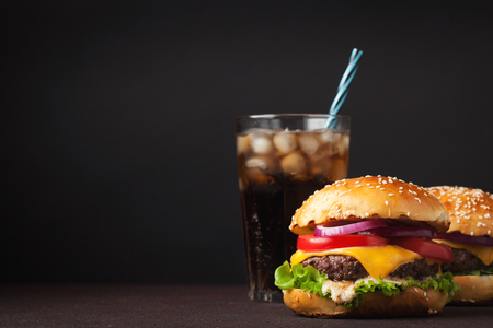 Close-up of delicious fresh home made burger with lettuce, cheese, onion, tomato and cola with ice on a dark background with copy space.の写真素材