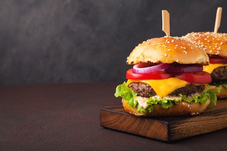 Close-up of delicious fresh home made burger with lettuce, cheese, onion and tomato on a dark background with copy space. fast food and junk food concept.の写真素材