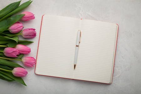 Blank note pad with pen and pink tulips on light stone background.の写真素材