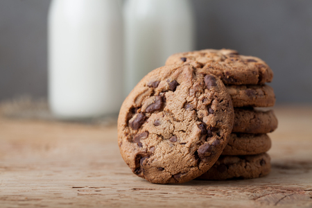 A stack of cookies with milk chocolate and two bottles of milk on a wooden table.の写真素材