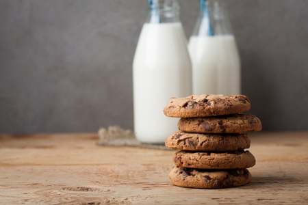 A stack of cookies with milk chocolate and two bottles of milk on a wooden table.の写真素材