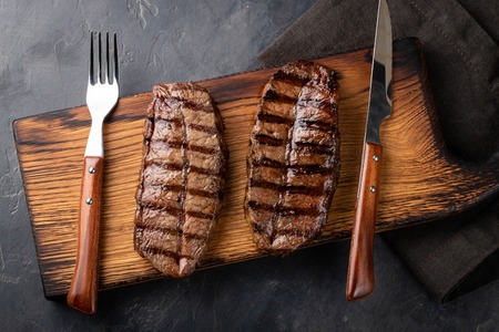 Closeup ready to eat steak Top Blade beef breeds of black Angus with grill tomato, garlic and on a wooden Board. The finished dish for dinner on a dark stone background. Top viewの写真素材