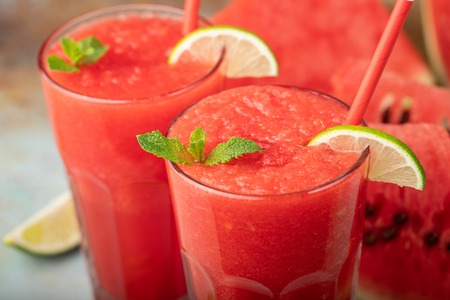 Watermelon slushie with lime, summer refreshing drink in tall glasses on a blue rusty background.の写真素材