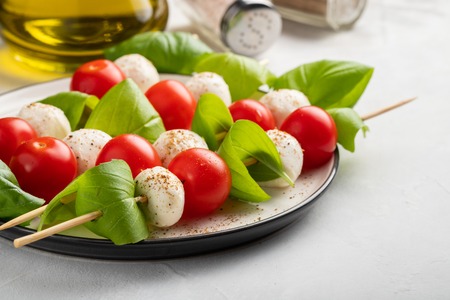 Caprese salad - skewer with tomato, mozzarella and basil, italian food and healthy vegetarian diet concept on a light background.の写真素材