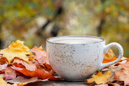 Autumn, fall leaves, hot steaming cup of coffee on wooden table background. Seasonal, morning...