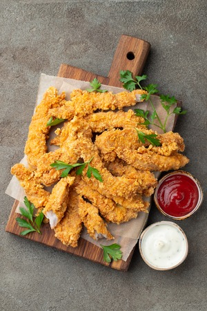 Breaded chicken strips with two kinds of sauces on a wooden Board. Fast food on dark brown background. Top view.の写真素材