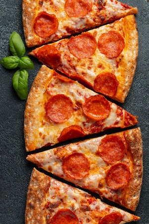 Tasty pepperoni pizza and cooking ingredients tomatoes basil on black concrete background. Top view of hot pepperoni pizza. Flat lay.の写真素材