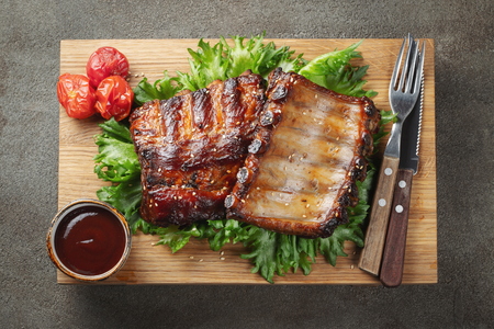 Closeup of pork ribs grilled with BBQ sauce and caramelized in honey on a bed of salad frisse. Tasty snack to beer on a wooden Board for filing on dark concrete background. Top view. Flat lay.の写真素材