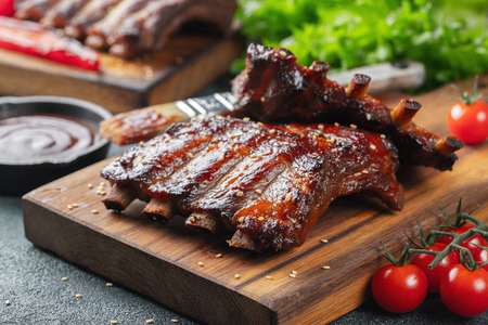 Closeup of pork ribs grilled with BBQ sauce and caramelized in honey. Tasty snack to beer on a wooden Board for filing on dark concrete background.の写真素材
