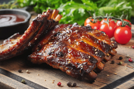 Closeup of pork ribs grilled with BBQ sauce and caramelized in honey. Tasty snack to beer on a wooden Board for filing on dark concrete backgroundの写真素材