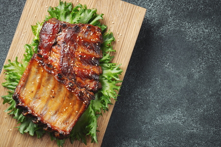 Closeup of pork ribs grilled with BBQ sauce and caramelized in honey. Tasty snack to beer on a paper for filing on dark concrete background. Top view with copy space. Flat layの写真素材
