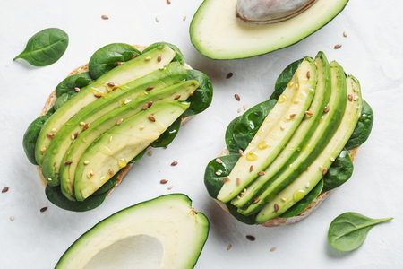Two ciabatta toast with sliced avocado olive oil, spinach and flax and sesame seeds. Healthy...