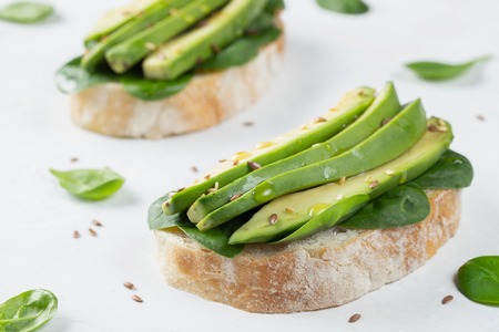 Two ciabatta toast with sliced avocado olive oil, spinach and flax and sesame seeds. Healthy vegetarian Breakfast on white backgroundの写真素材