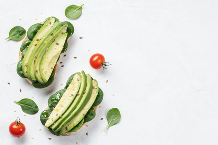 Two ciabatta toast with sliced avocado olive oil, spinach and flax and sesame seeds. Healthy vegetarian Breakfast on white background with copy space. Top view. Flat layの写真素材