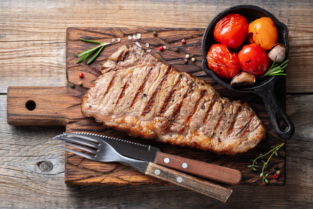 Steak Striploin, grilled with pepper, garlic, salt and thyme served on a wooden board. The finished dish for dinner on a old wooden rustic table. Top view.の写真素材