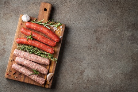 Assorted fresh sausages with thyme, rosemary, olive oil and garlic on a wooden chopping board on a dark concrete table. Ready to cook sausages for dinner on brown background. Top view with copy space.の写真素材