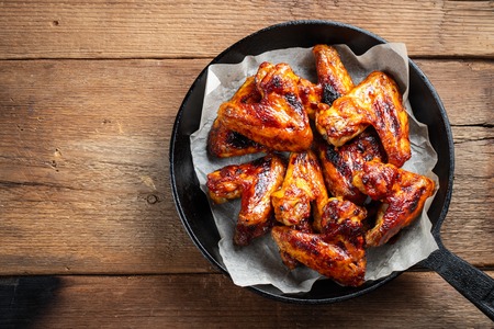 Baked chicken wings in barbecue sauce in a cast iron pan on an old wooden rustic table. Top view with copy space.の写真素材
