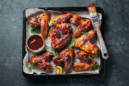 Roasted chicken wings in barbecue sauce with sesame seeds and parsley in a baking tray on a dark table. Top view. Tasty snack for beer on a dark background. Flat lay.の写真素材