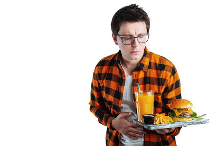 A young man suffering from stomach pain holding burger isolated on white background.の写真素材