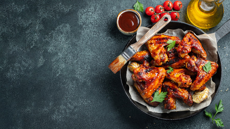 Baked chicken wings in barbecue sauce with sesame seeds and parsley in a cast iron pan on a dark concrete table. Top view with copy spaceの写真素材