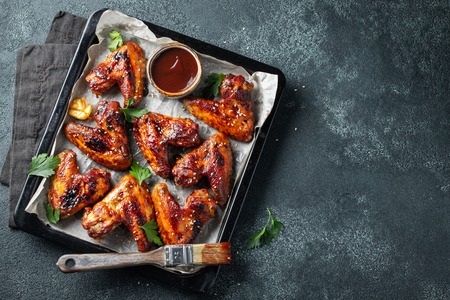 Roasted chicken wings in barbecue sauce with sesame seeds and parsley in a baking tray on a dark table. Top view with copy space. Tasty snack for beer on a dark background. Flat lay.の写真素材