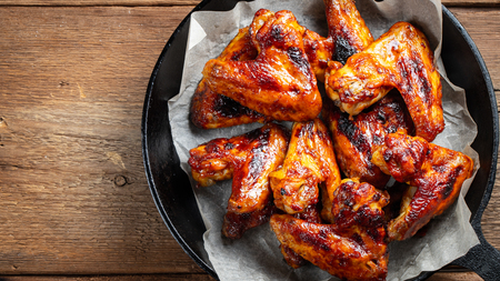 Baked chicken wings in barbecue sauce in a cast iron pan on an old wooden rustic table. Top view with copy space.の写真素材
