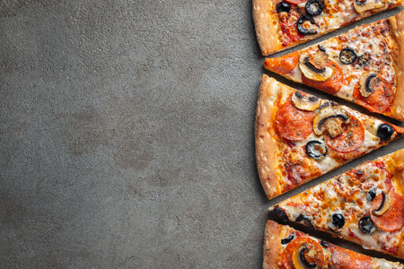 Cut into slices delicious fresh pizza with sausage pepperoni and cheese on a dark background. Top view with copy space for text. Pizza on the black concrete table. flat lay.の写真素材