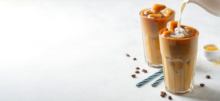 Ice coffee in a tall glass with cream poured over and coffee beans. Cold summer drink on a light background. With copy space.の写真素材