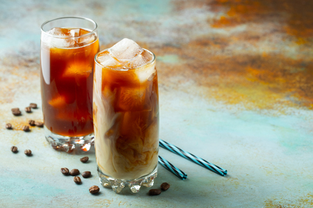 Ice coffee in a tall glass with cream poured over and coffee beans. Cold summer drink on a blue rusty background with copy spaceの写真素材