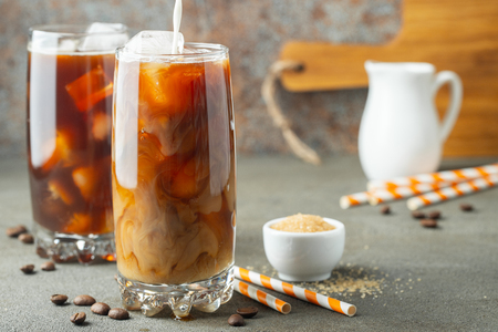 Ice coffee in a tall glass with cream poured over and coffee beans. Cold summer drink on a brown rusty background.の写真素材