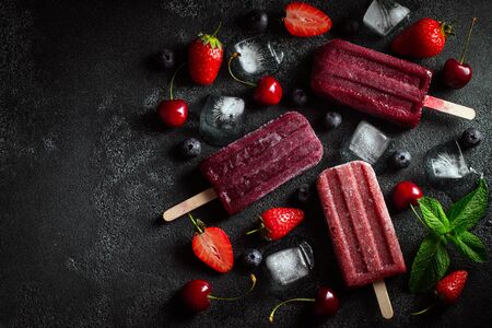Bright ice lolly made of cherries, strawberries and blueberries on a dark concrete background. Sweet summer treat. Top view with copy space. Flat layの写真素材