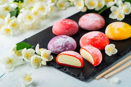 Multi-colored Japanese ice cream Mochi in rice dough and Jasmine flowers on a concrete blue background. Traditional Japanese dessert on a black slate.の写真素材