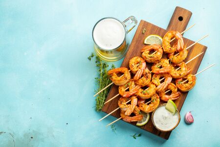 Grilled shrimp skewers or langoustines served with lime, garlic and sauce on a light blue concrete background. Seafood and beer. Top view with copy space. Flat lay.の写真素材