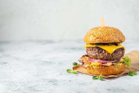 homemade delicious burger of beef, bacon, cheese, lettuce and tomatoes on a light concrete background. Fat unhealthy food close-up. With copy space.の写真素材