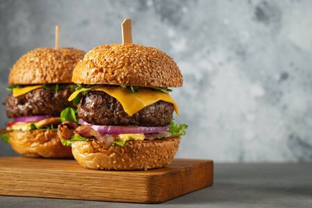 A set of homemade delicious burgers of beef, bacon, cheese, lettuce and tomatoes on a light concrete background. Fat unhealthy food close-up. With copy space.の写真素材