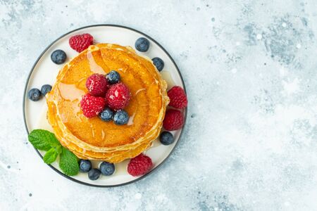 Close-up delicious pancakes, with fresh blueberries, raspberrys and honey on a light background. Top...
