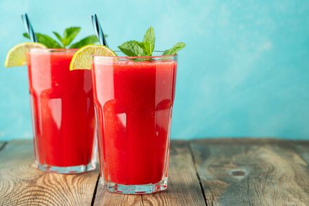 Watermelon slushie with lime and mint, summer refreshing drink in tall glasses on a light blue background. Sweet cold smoothie with copy space.の写真素材