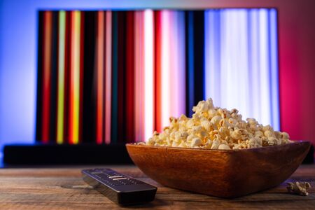 A wooden bowl of popcorn and remote control in the background the TV works. Evening cozy watching a movie or TV series at home.の写真素材