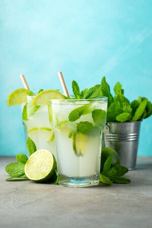 Two homemade lemonade or mojito cocktail with lime, mint and ice cubes in a glass on a light stone table. Fresh summer drinkの写真素材