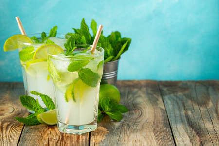 Two homemade lemonade or mojito cocktail with lime, mint and ice cubes in a glass on a wooden rustic table. Fresh summer drink. With copy space.の写真素材