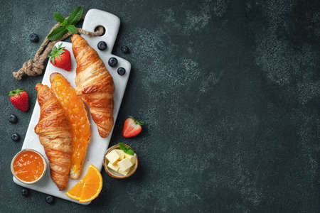 Fresh sweet croissants with butter and orange jam for breakfast. Continental breakfast on a black concrete table. Top view with copy space. Flat layの写真素材