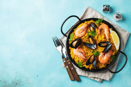 Traditional spanish seafood paella in pan with chickpeas, shrimps, mussels, squid on light blue concrete background. Top view with copy spaceの写真素材